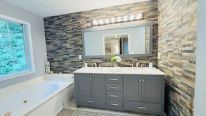 Un baño moderno con salpicadero de piedra, un espejo grande, tocador doble y bañera.
