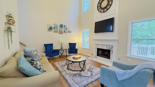 Una sala de estar con un sofá beige, sillones azules, una mesa de centro y una chimenea.