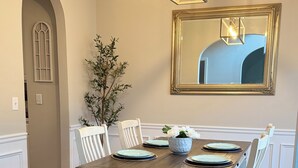 Un comedor con una mesa de madera, sillas blancas, un tapete azul y una araña.