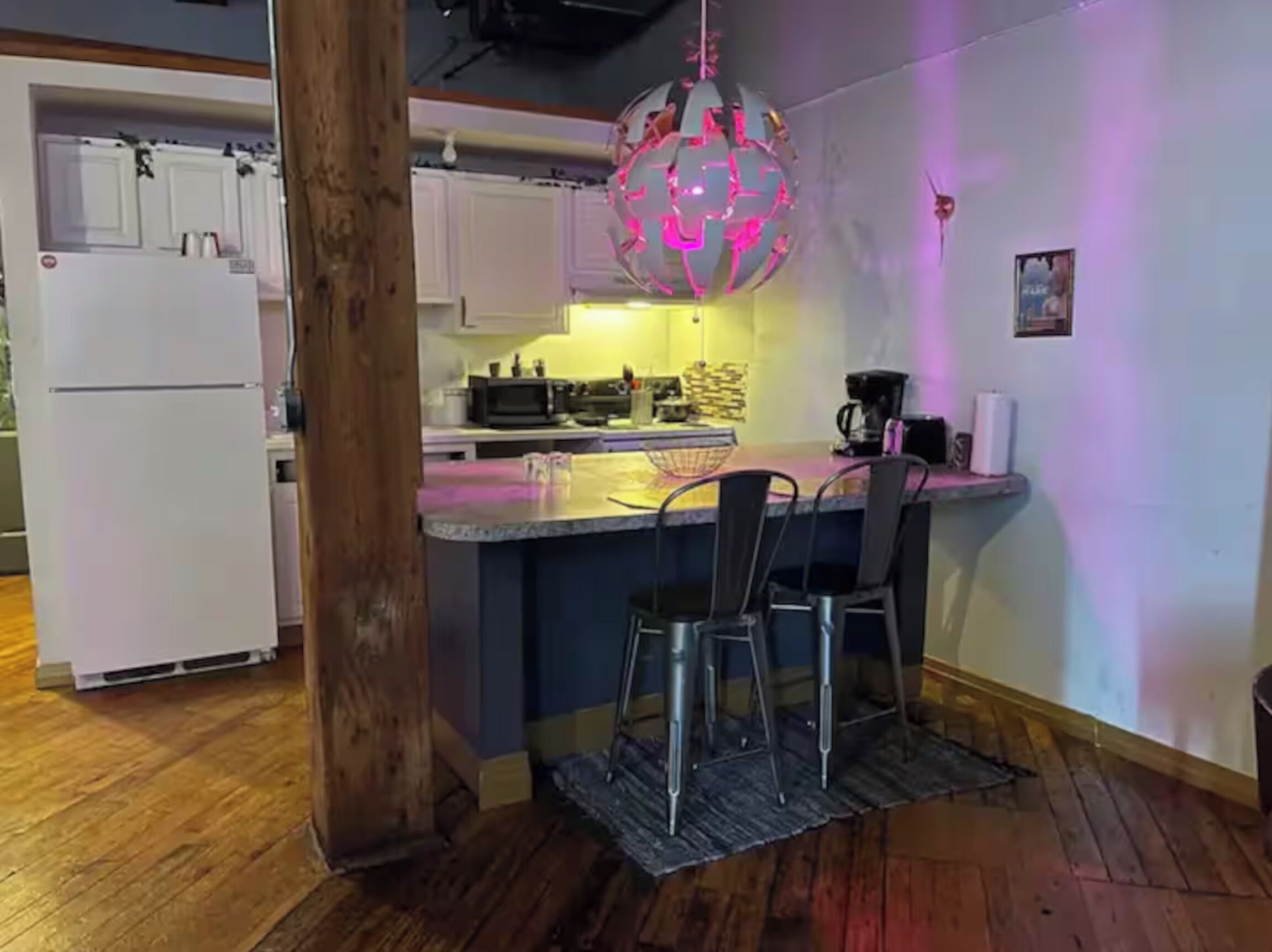 A compact kitchen with a central island, a refrigerator, and a hanging light fixture.