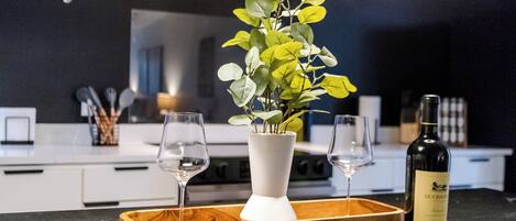 A modern kitchen with a white vase containing green leaves, two wine glasses on a wooden tray, and a bottle of Duckhorn wine on the counter.