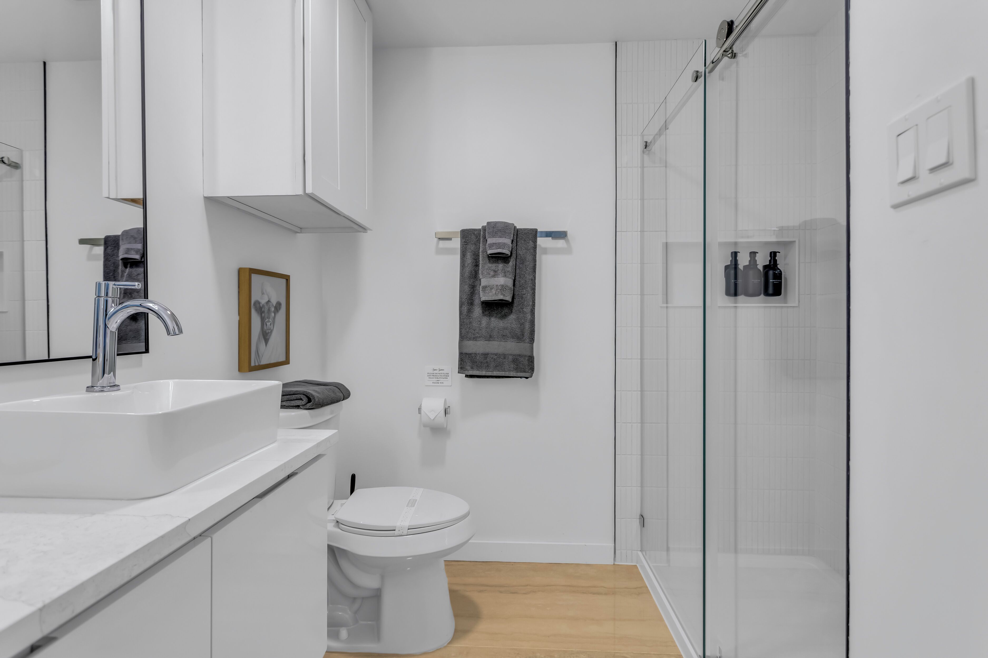 Une salle de bain moderne avec un lavabo blanc, des toilettes et une douche à parois de verre.