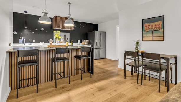 Et moderne køkken med en central ø, barstole og et spisebord med stole.