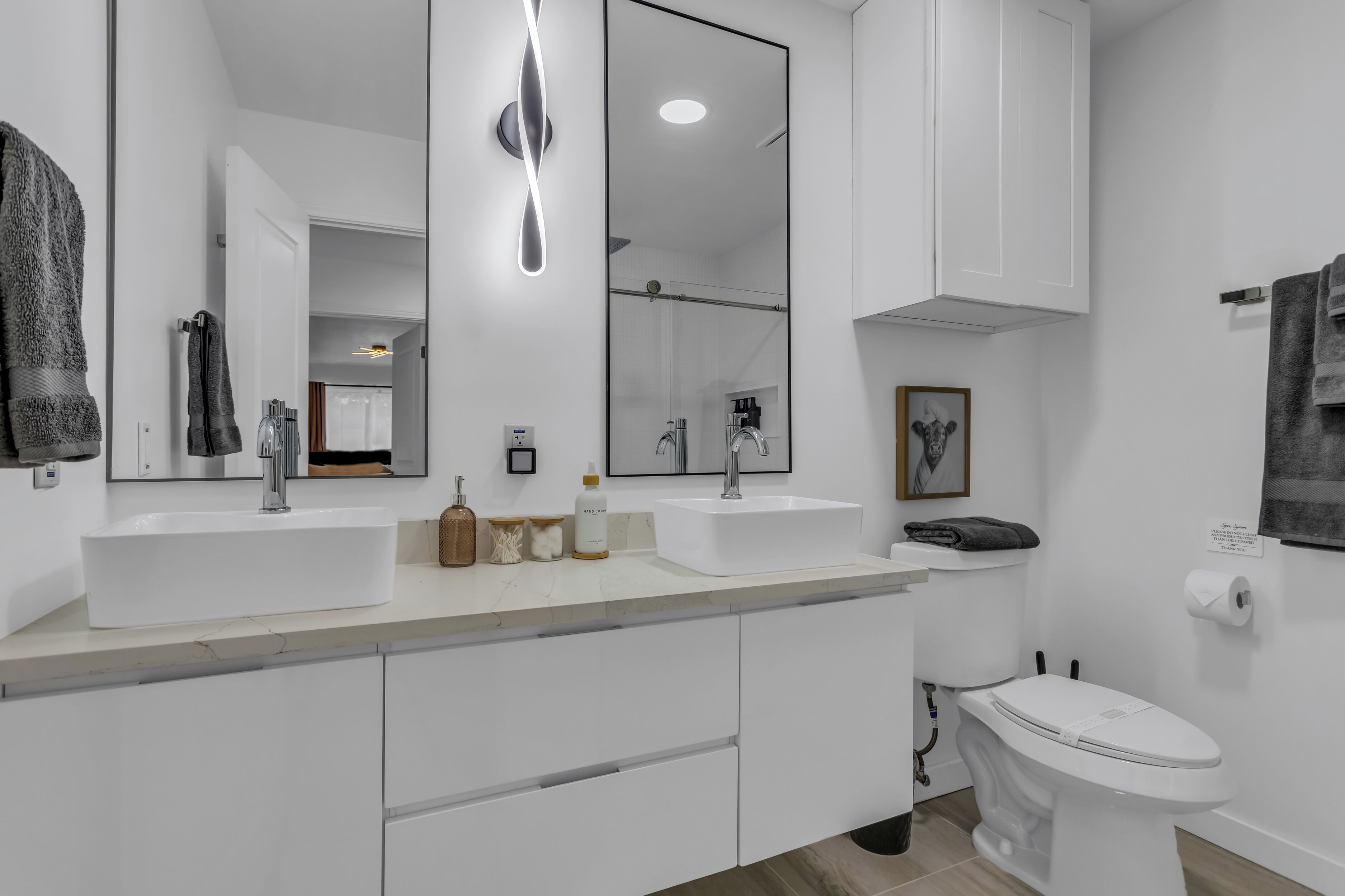 A modern bathroom with two sinks, a large mirror, and a toilet.