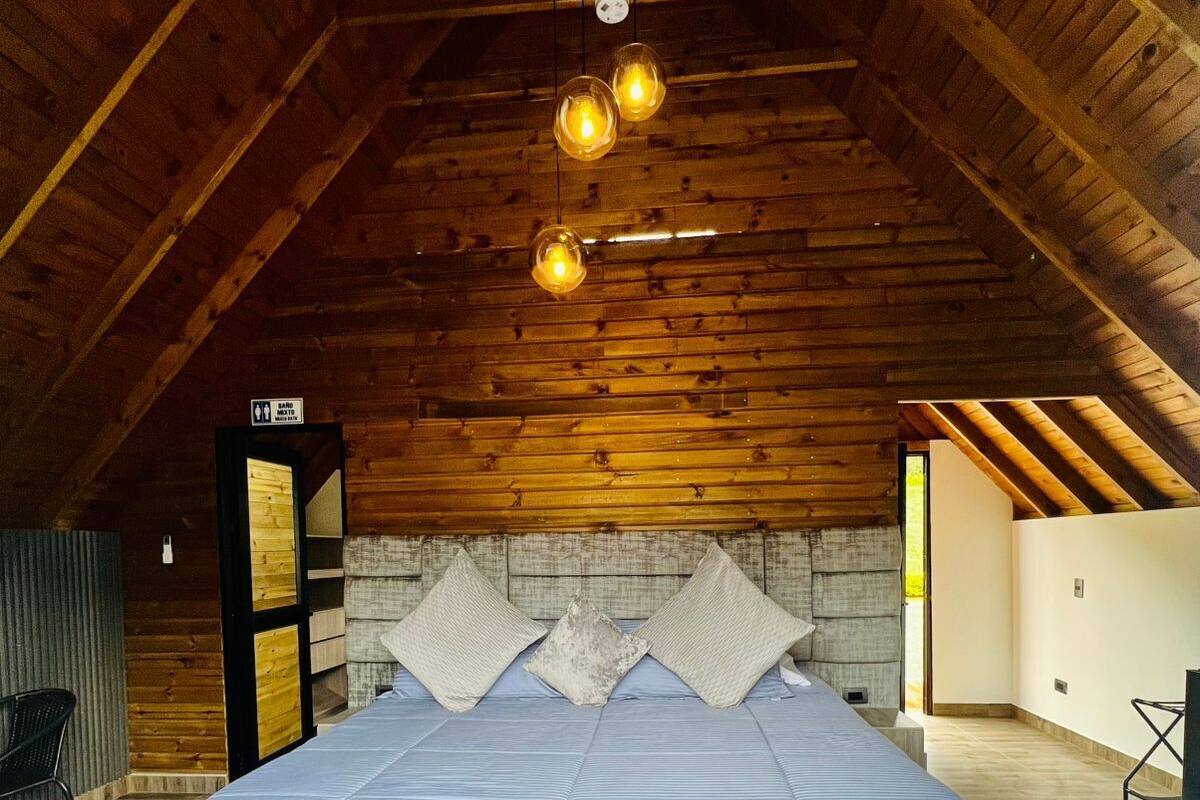 A bedroom with a large bed, wooden ceiling beams, and a stone wall.