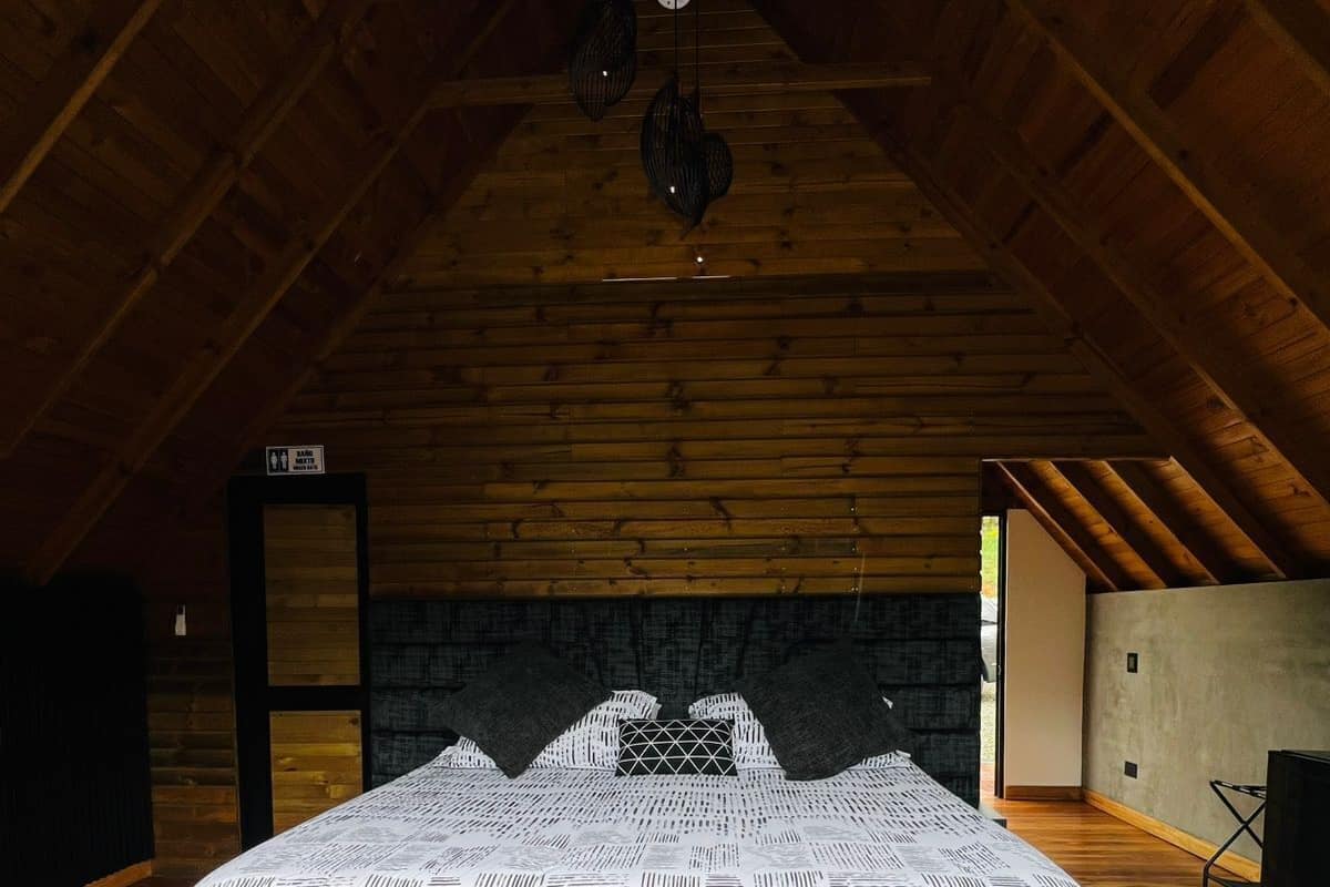 A bedroom with a large bed, wooden beams, a stone wall, and a small window.