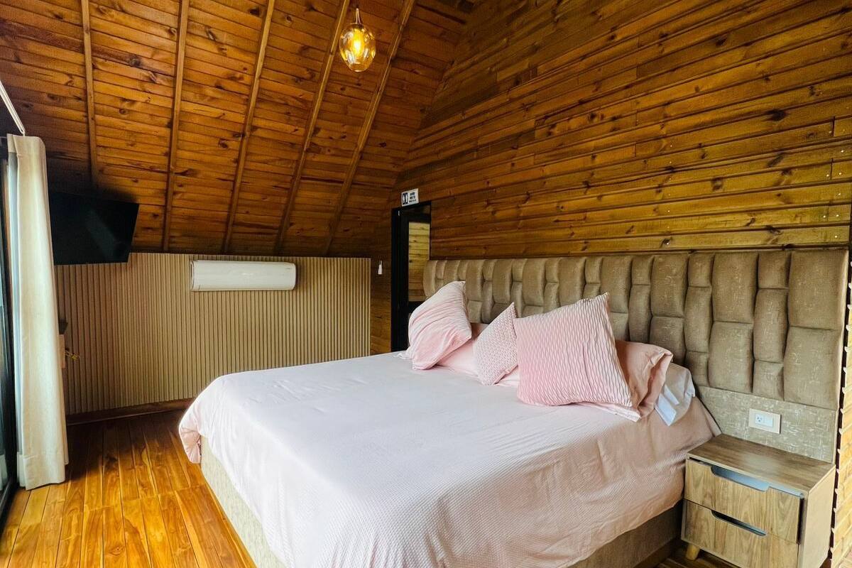 A wooden cabin bedroom with a bed, bedside table, and hanging light fixtures.
