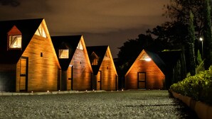 A row of wooden cabins with pitched roofs, each featuring a small window and a door, illuminated by warm lighting against a dark sky. - Hotel Noral Lemont (Copacabana)