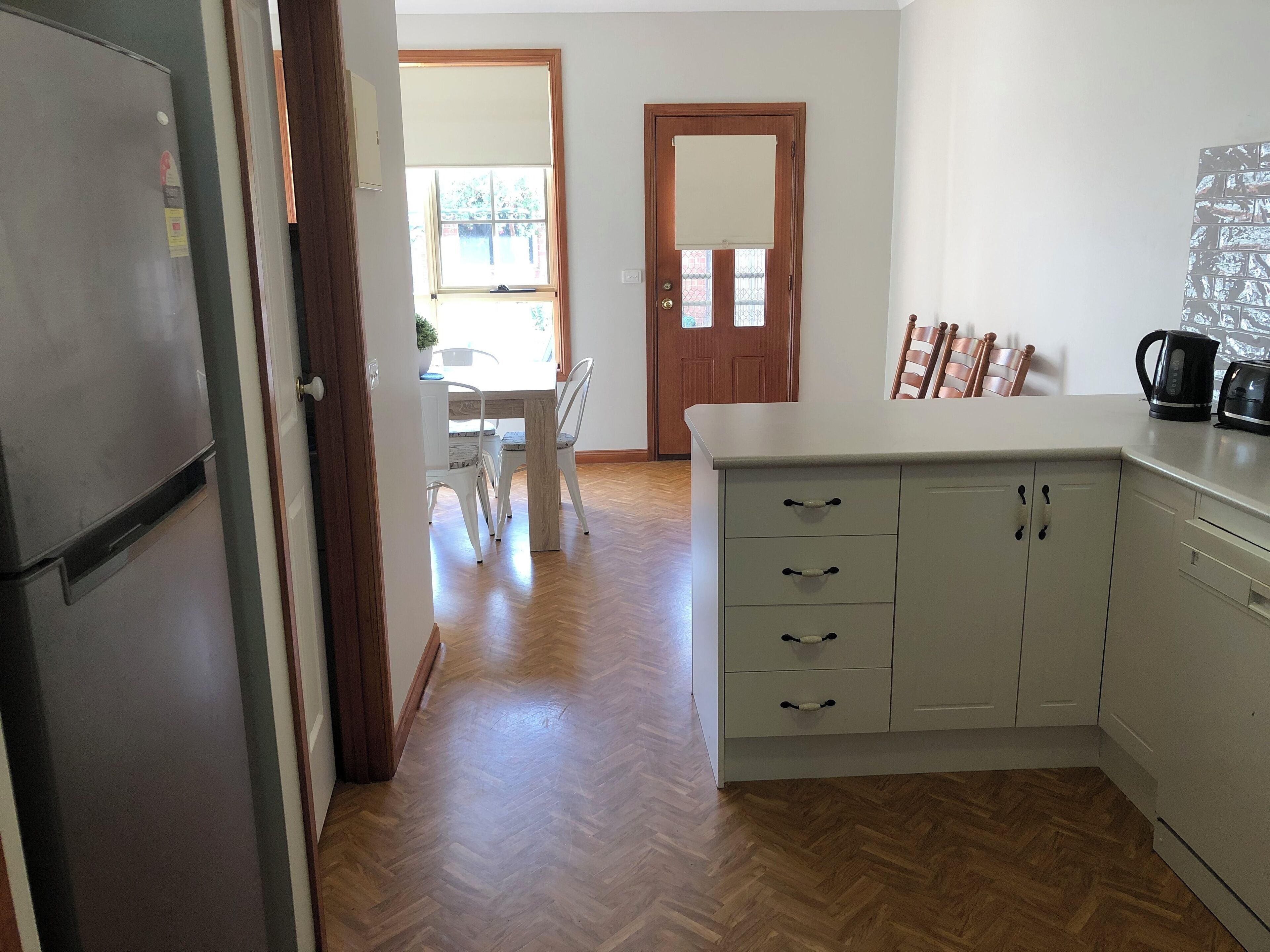 A kitchen with a refrigerator, white cabinets, and a coffee maker.