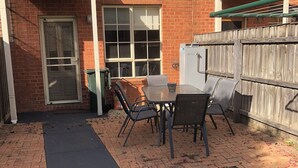 A brick building with a patio area featuring a table and chairs, a green awning, and a wooden fence.
