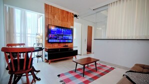 A living room with a TV, wooden entertainment unit, a dining table with chairs, and a checkered rug. - Entire Apartment (Paulo VI Belo Horizonte)