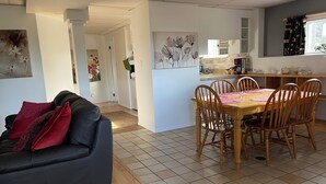 A modern living room with a dark sofa, a wooden dining table with six chairs, and a kitchen area with a window and various appliances. - Nice 2-bedroom walk-in lower suite in Salmon Arm. Private parking and yard. (Salmon Arm)