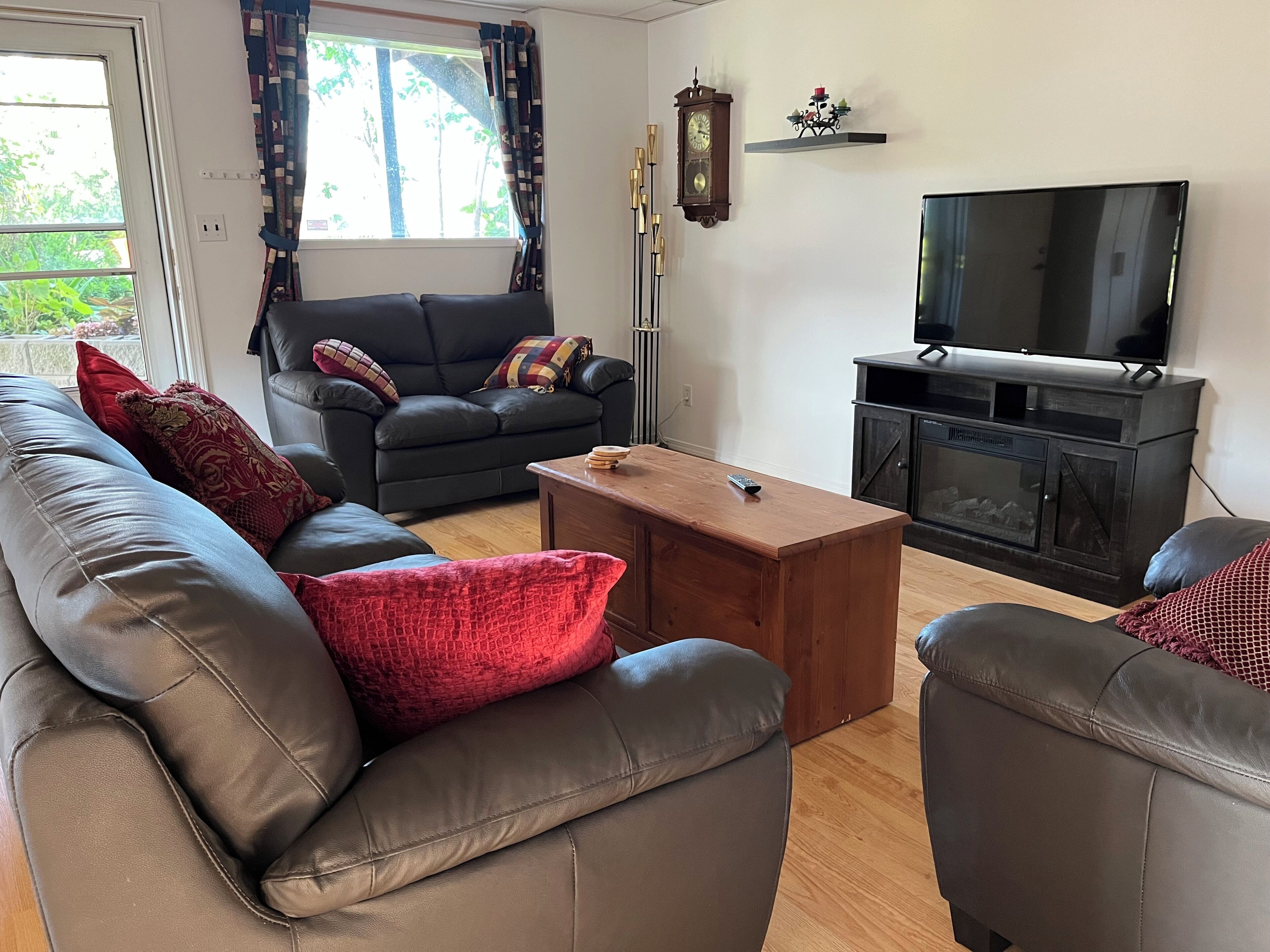 A living room with a sofa, armchair, coffee table, TV, fireplace, and a clock on the wall.