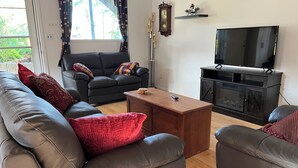 A living room with a sofa, armchair, coffee table, TV, fireplace, and a clock on the wall. - Nice 2-bedroom walk-in lower suite in Salmon Arm. Private parking and yard. (Salmon Arm)