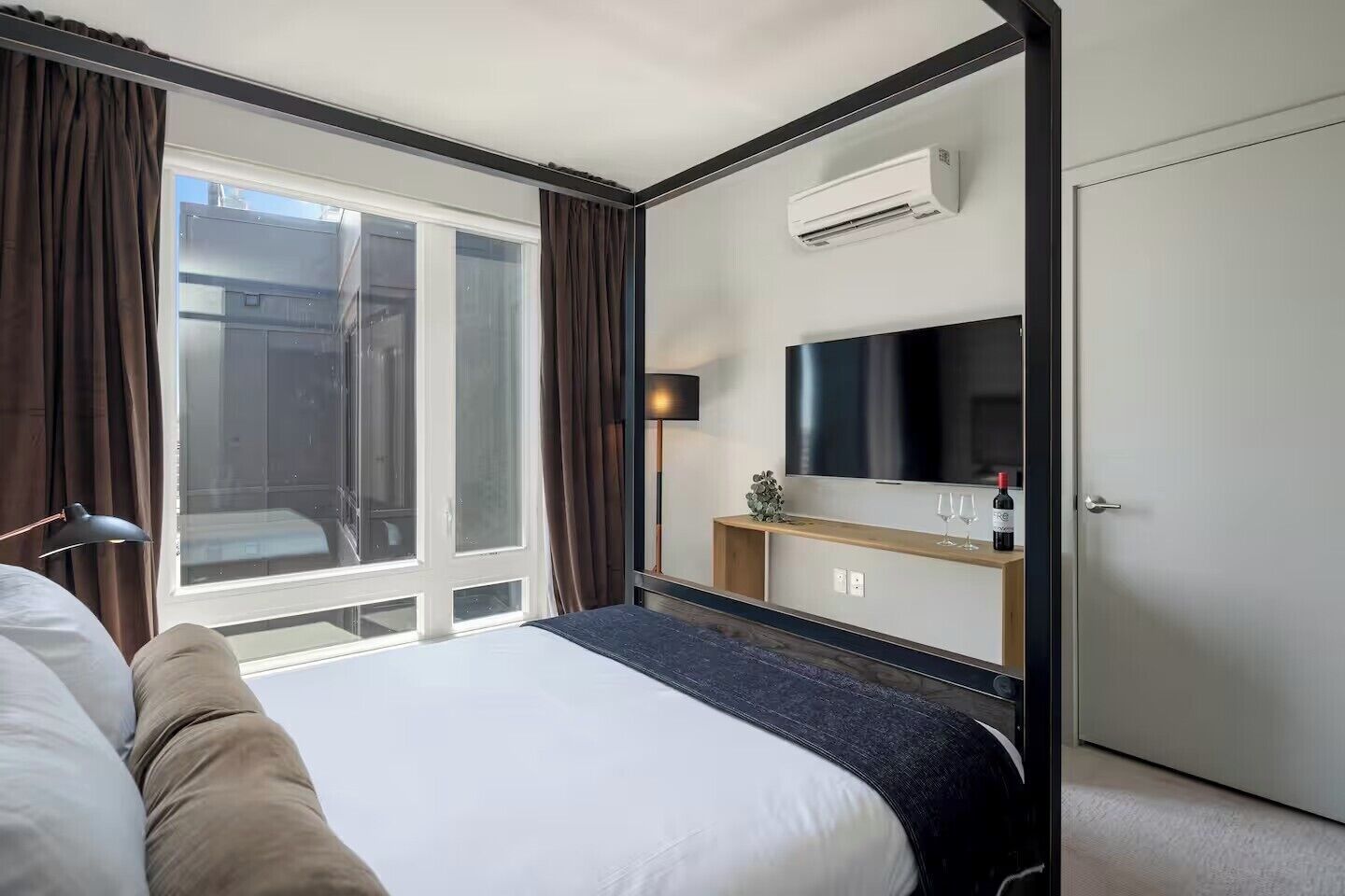 A hotel room with a bed, a TV, a minibar, and a window with curtains.