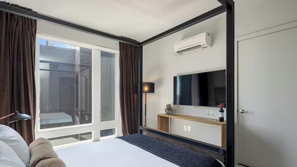 Quarto de hotel com cama, televisão, minibar e janela com cortinas.