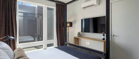 A hotel room with a bed, a TV, a minibar, and a window with curtains.