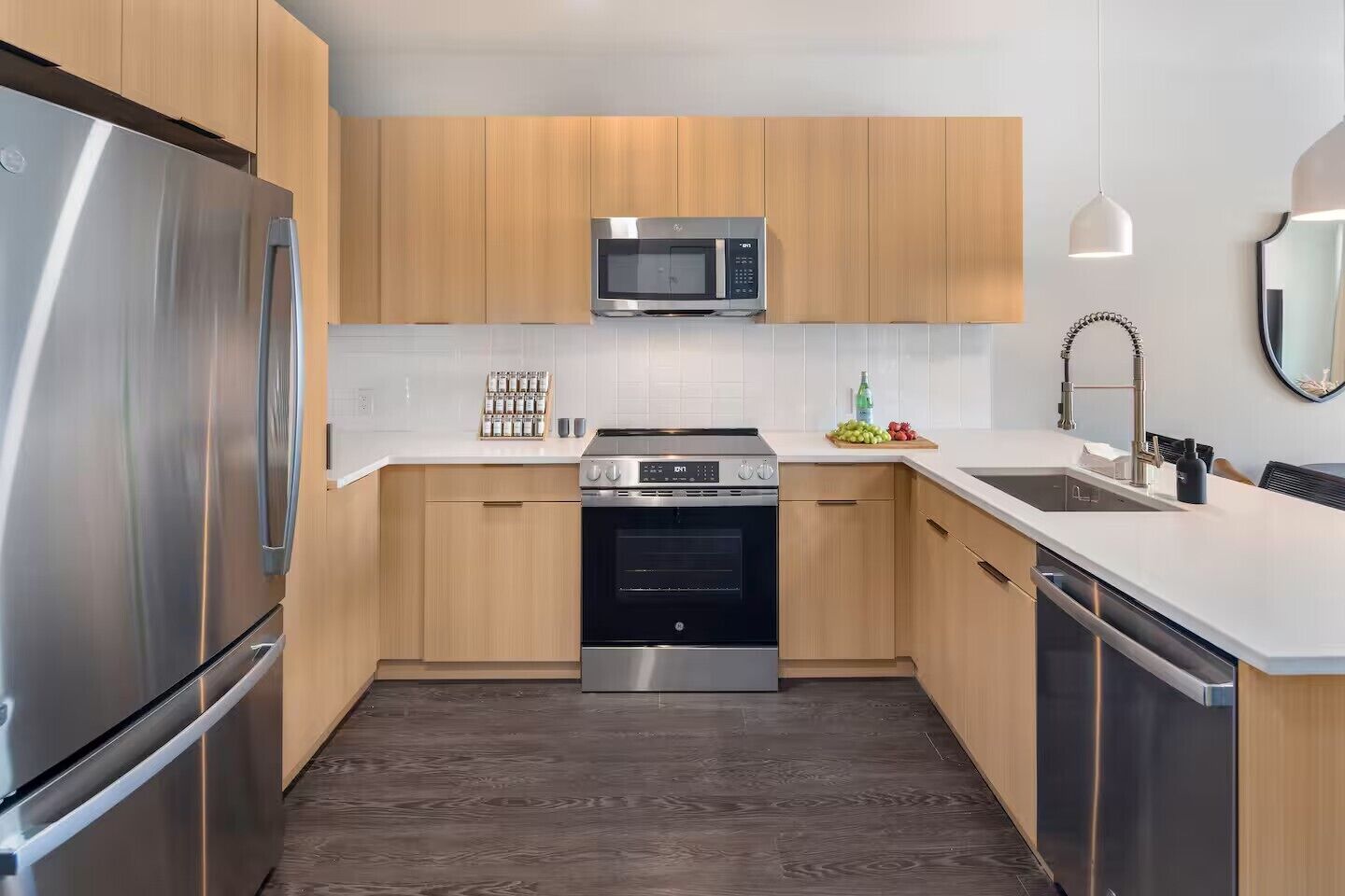 Una cocina moderna con electrodomésticos de acero inoxidable, armarios de madera y encimera blanca.