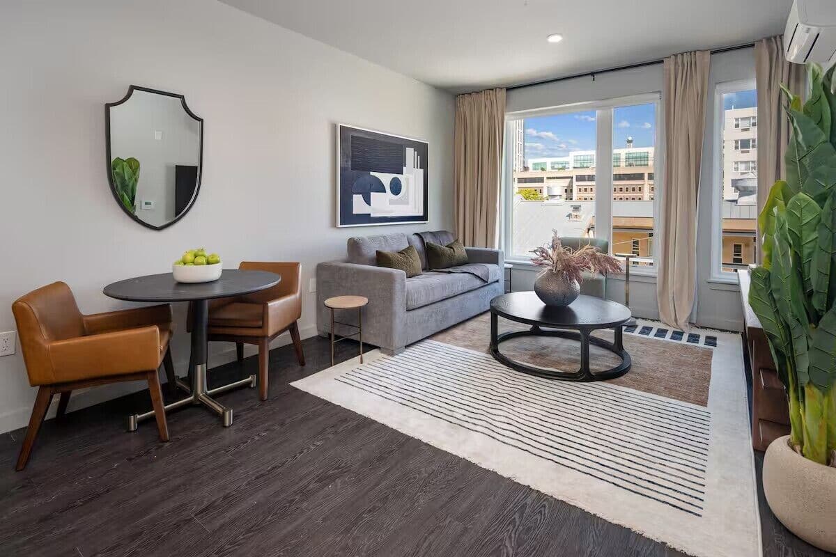 Un salon moderne avec un canapé gris, une table basse ronde et un coin repas comprenant une table et des chaises.
