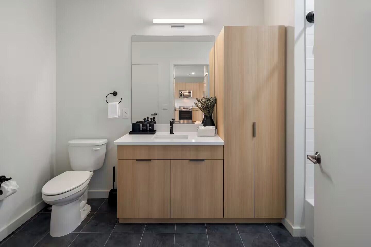 A modern bathroom with a toilet, sink, mirror, and wooden cabinets.