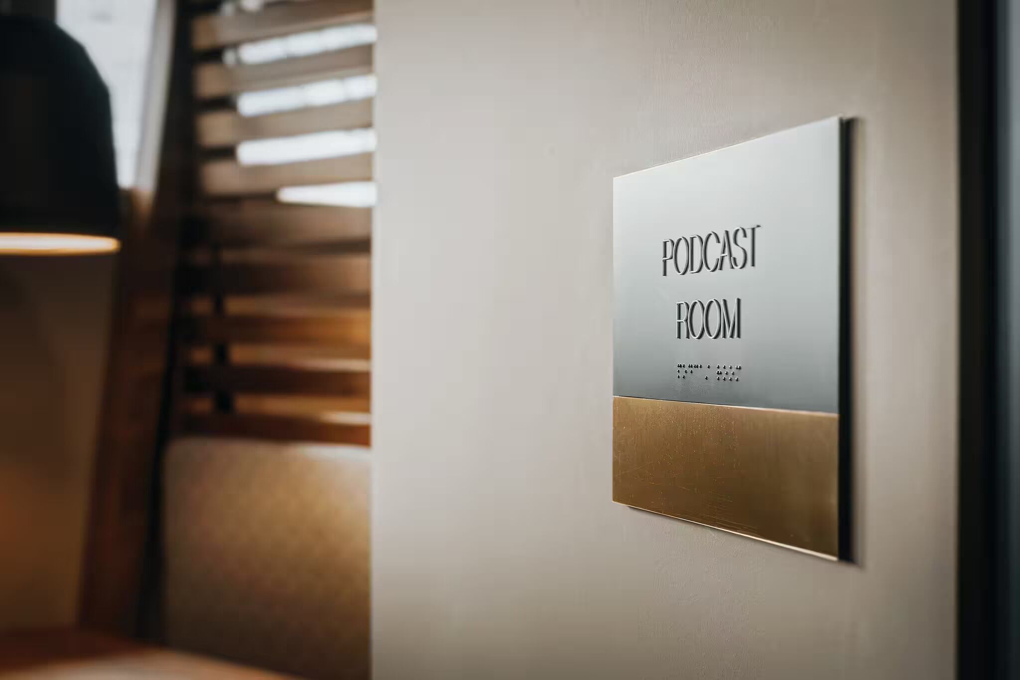 Ein Schild, das auf einen Podcast-Raum hinweist, mit modernem Design und einem Lamellenfenster im Hintergrund.
