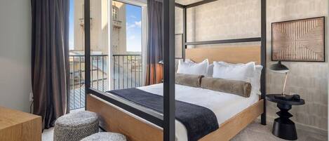 Une chambre d’hôtel moderne avec un lit à baldaquin, un balcon offrant une vue agréable et une petite table d’appoint avec une lampe.