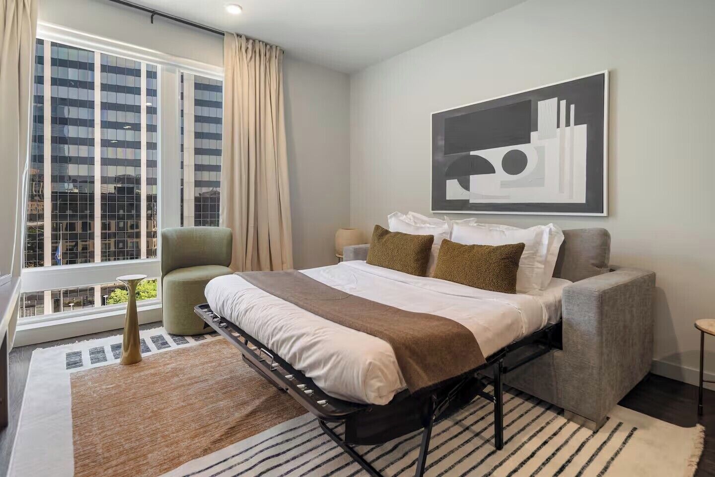 Ein modernes Hotelzimmer mit einem Bett, einem Sessel, einem kleinen Tisch und einem großen Fenster mit Vorhängen.