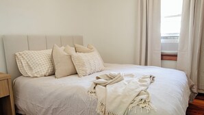 Ein ordentlich bezogenes Bett mit einem beigefarbenen Karokissen, einem gemusterten Kissen und einer weißen Tagesdecke.