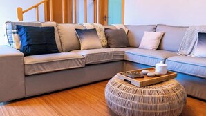 Una sala de estar moderna con un sofá modular, un taburete redondo tejido y una bandeja con piedras y una vela.