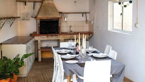 Comedor con una mesa preparada para cuatro personas, suelo de ladrillo y cocina al fondo.