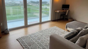 Una sala de estar moderna con un amplio ventanal corredizo que da a un balcón, un sofá, un televisor y una pequeña mesa.