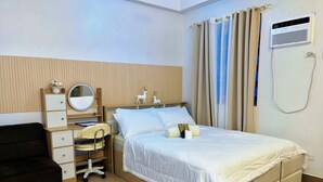 A hotel room with a bed, a desk with a chair, a dresser, a mirror, and a window with curtains.
