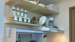 A modern kitchen with a black countertop, stainless steel sink, and a built-in oven. There are shelves above the counter holding kitchen utensils and appliances.