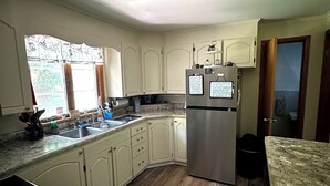 Una cocina con gabinetes blancos, un refrigerador de acero inoxidable, un lavamanos y un ventanal con cortinas.
