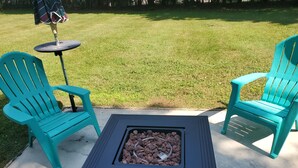 Un patio con dos sillas turquesa, una mesa redonda pequeña y una mesa cuadrada con un hogar para fuego.