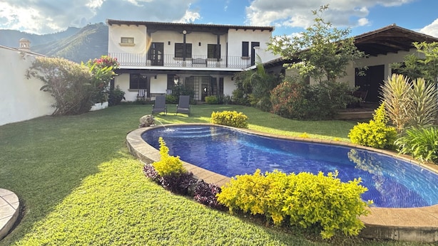 Una casa de dues plantes amb piscina, envoltada de gespa ben cuidada i diferents plantes.