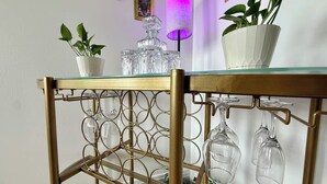 A glass-top table with a gold metal frame, holding a crystal decanter, a potted plant, and several wine glasses. - Downtown: The Belle Isle View Loft (Detroit)
