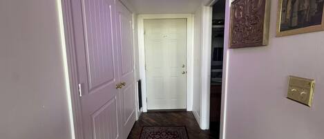 A hallway with a wooden floor, a patterned rug, a white door, and a wall with a framed picture.