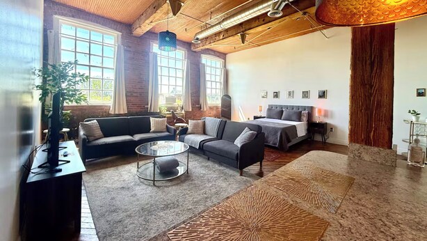 A spacious living room with a large window, a sofa, a coffee table, and a bed. - Downtown: The Belle Isle View Loft (Detroit)