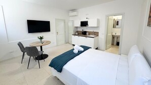 Une chambre d’hôtel moderne équipée d’un lit, d’un bureau avec une chaise, d’une télévision, d’une kitchenette et d’une salle de bain.