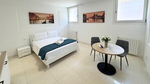 Une chambre d’hôtel avec un lit, une table ronde et deux chaises, ainsi que deux fenêtres.