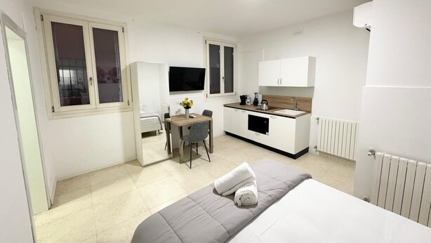 A compact hotel room with a bed, a small kitchenette, a dining area, and a TV.
