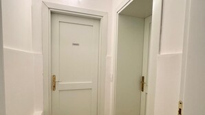 A narrow hallway with a closed door, a light fixture on the ceiling, and a carpeted floor.