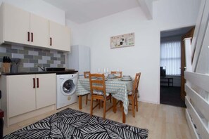 A compact kitchen with a washing machine, a dining table with chairs, and a patterned rug. - Cosy Studio Near Goodison & Anfield, Liverpool (Liverpool)