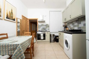 A compact kitchen with a dining table, chairs, a washing machine, and a small trash bin. - Cosy Studio Near Goodison & Anfield, Liverpool (Liverpool)