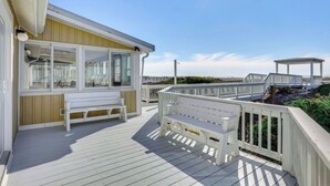 A wooden deck with white railings, a bench, and a small building with large windows.