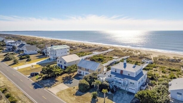 A coastal residential area with houses near the beach, featuring a clear view of the ocean and a road leading to the properties.