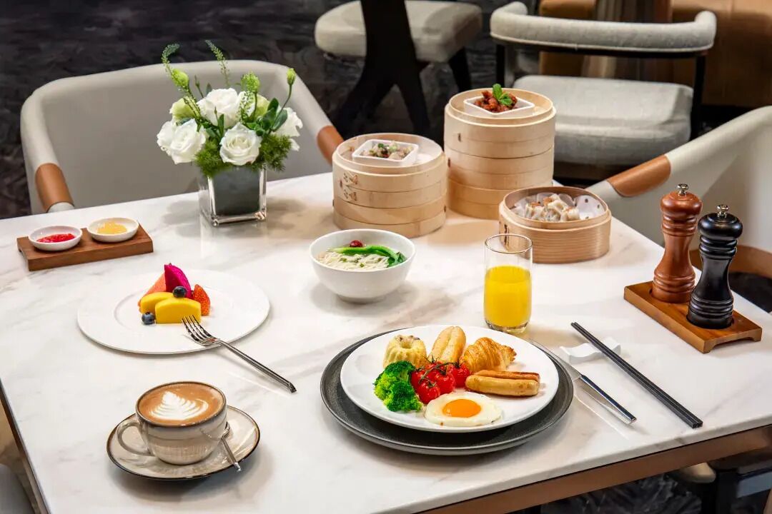 A breakfast setting with a variety of dishes, including eggs, vegetables, and pastries, along with a coffee cup and a glass of orange juice.