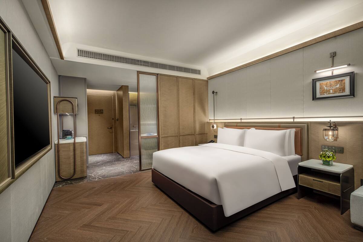 A hotel room with a large bed, a bedside table with a lamp, a wardrobe, and a mirror.