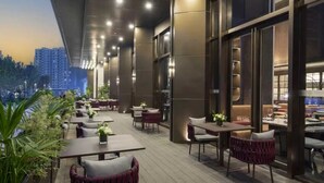 An outdoor dining area with tables and chairs, surrounded by plants and overlooking a cityscape. - Wanda Yi Hangzhou East Railway Station (Hangzhou)